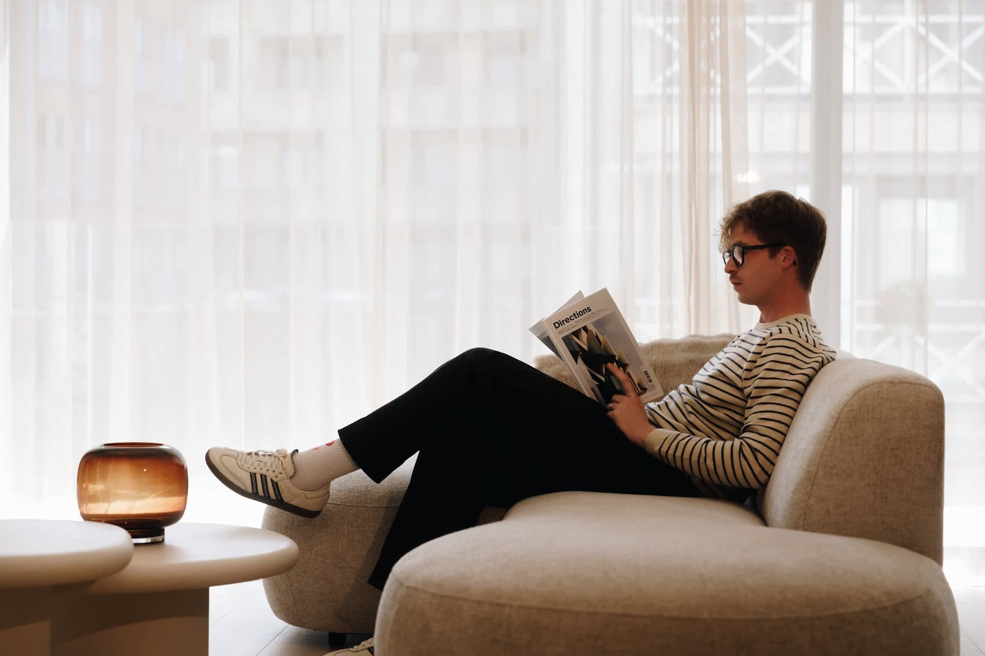 Someone reading a magazine on the sofa, lamp on the side table.