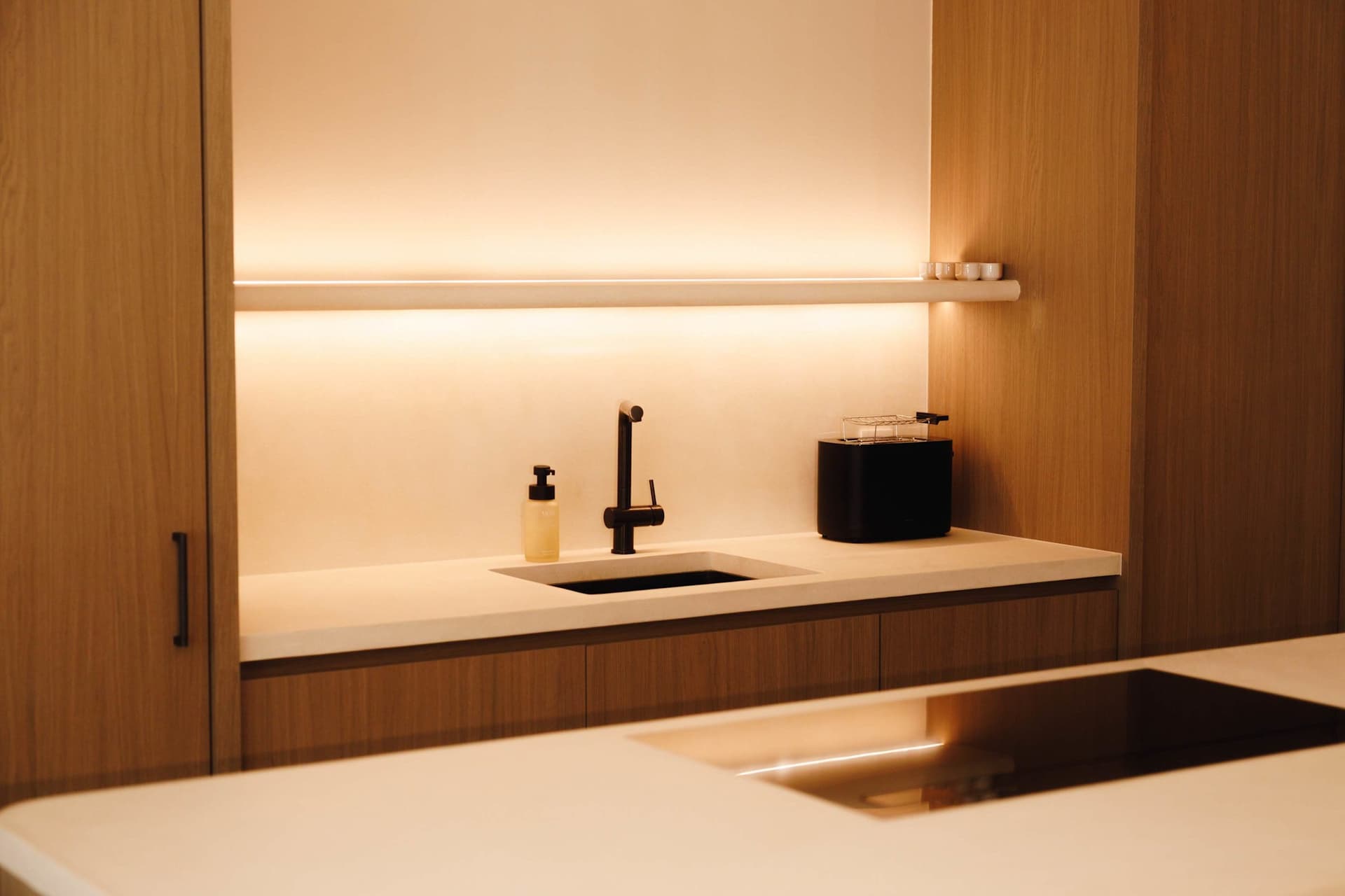 Wooden kitchen with induction hob and strip lighting.
