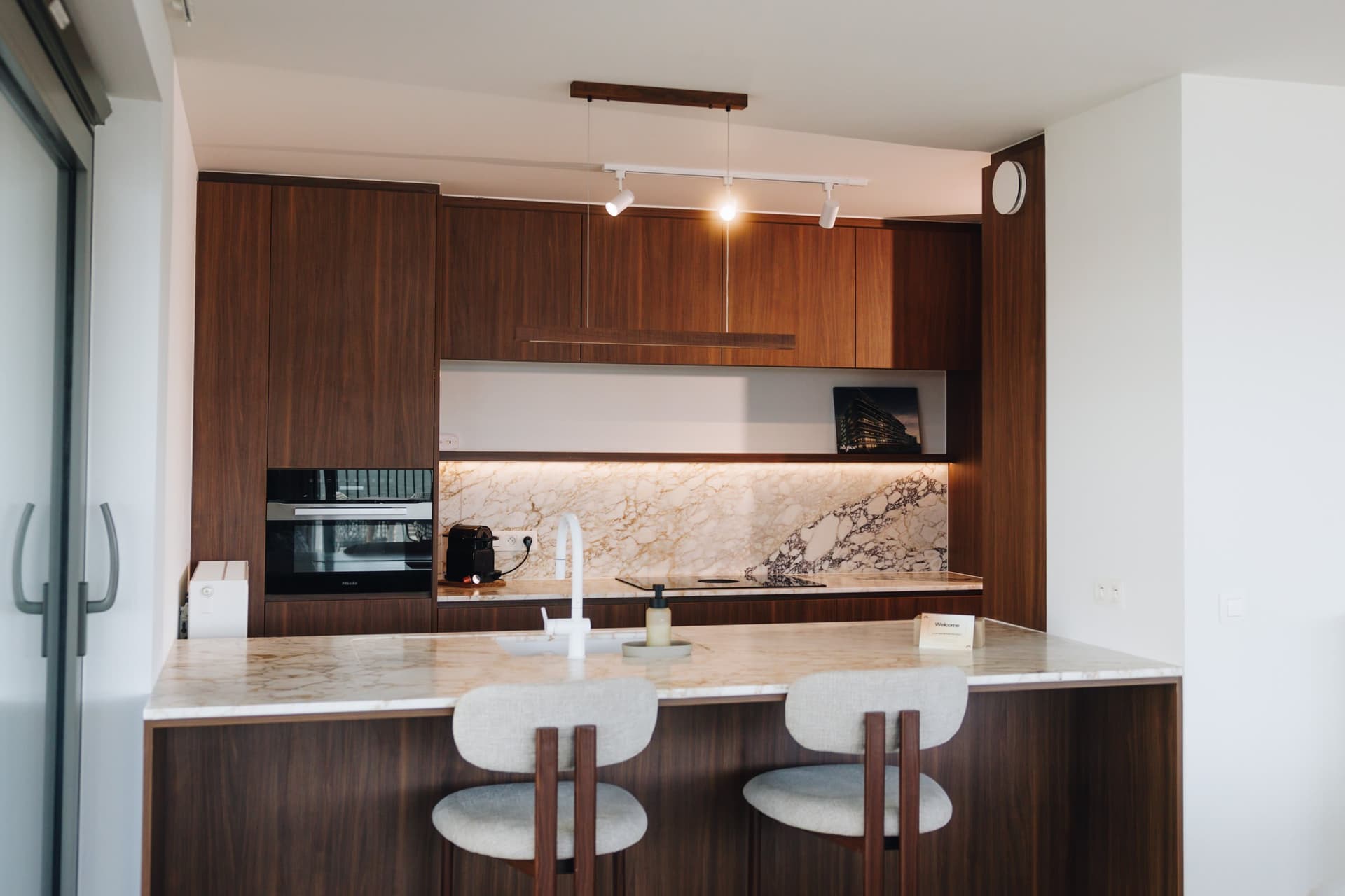 Keuken in hout met natuurstenen eiland en barkrukken.